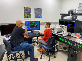 Two people sitting and talking next to a microscope 